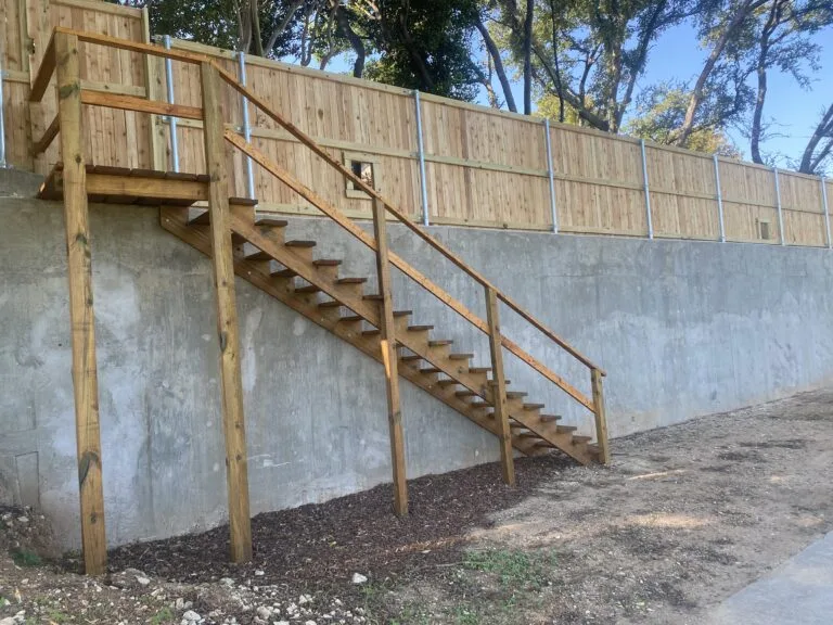 Poured concrete retaining wall with wood privacy fence and exterior wood staircase built on a sloped residential yard in Fort Worth TX