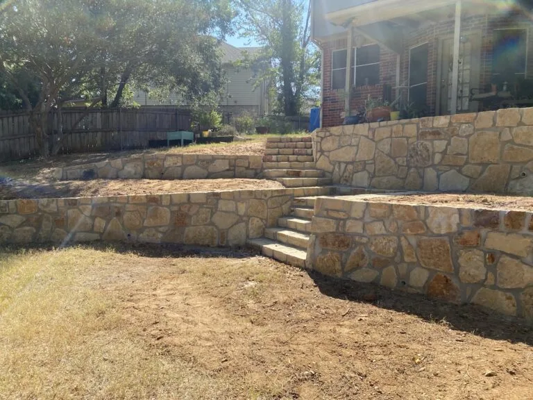 Multi-tier Milsap stone retaining walls with integrated stone steps connecting yard levels at a brick home in Arlington TX