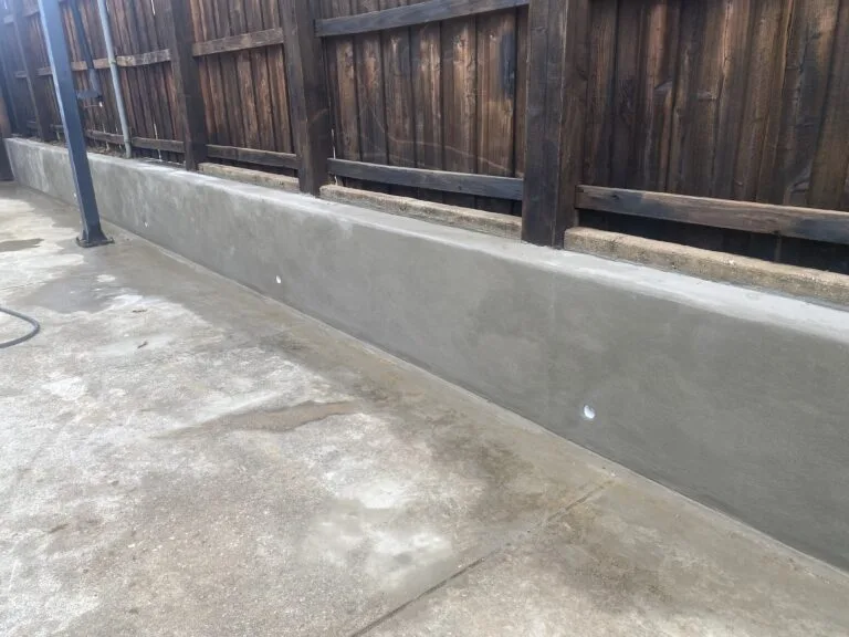 Freshly poured concrete retaining wall along wood privacy fence in North Richland Hills backyard, replacing old crosstie wall