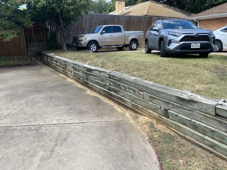 Aging weathered railroad timber retaining wall along residential driveway before replacement, Grand Prairie TX