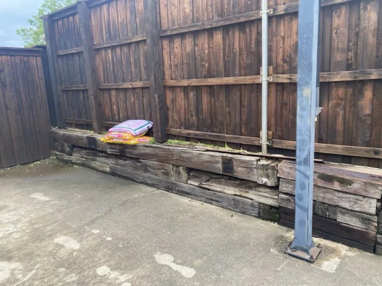 Deteriorating railroad tie retaining wall along wood privacy fence before replacement in North Richland Hills TX