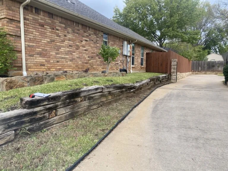 Failing railroad tie retaining wall along residential driveway in Bedford TX, rotting timbers leaning before replacement