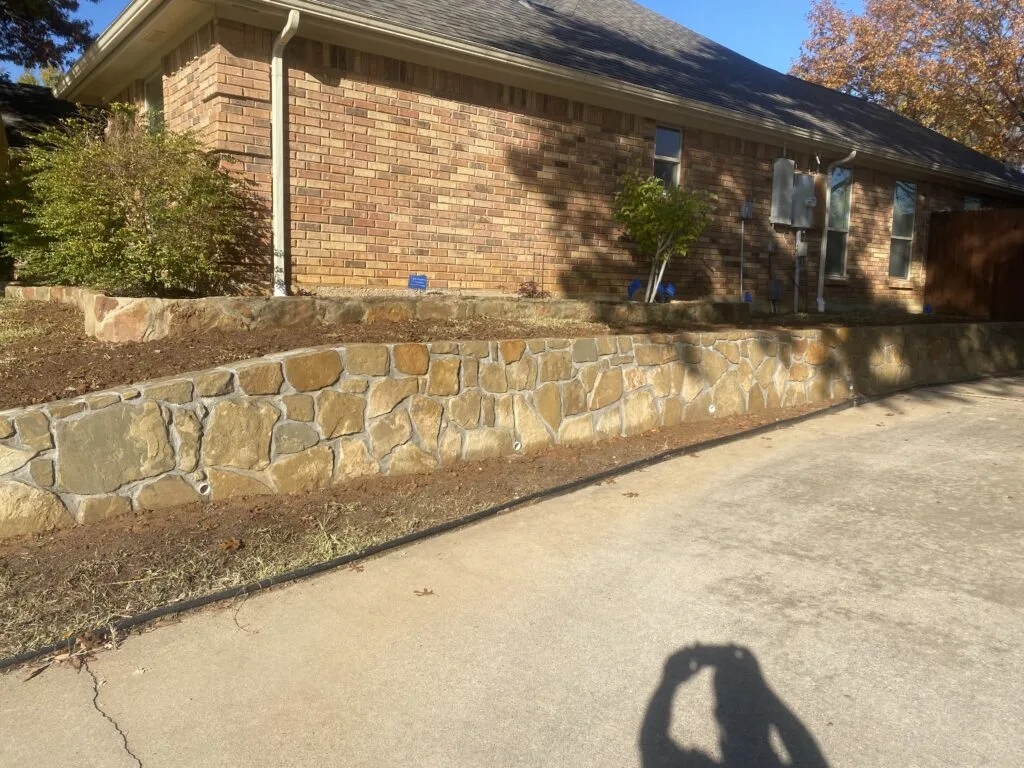 Completed Granbury stone retaining wall along driveway replacing old crosstie wall at brick home in Bedford TX