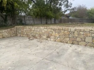 Granbury stone retaining wall replacing a failed wood crosstie wall along a concrete patio in a Fort Worth backyard