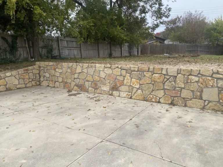 Granbury stone retaining wall replacing a failed wood crosstie wall along a concrete patio in a Fort Worth backyard