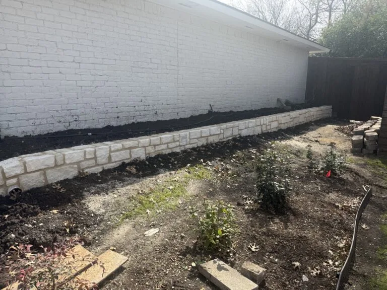 Newly built chopped Austin stone retaining wall along white brick home foundation in Dallas TX backyard