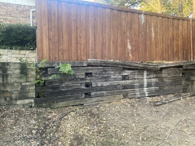 Failing railroad tie retaining wall bowing and separating beneath a wood fence in Highland Village TX, candidate for replacement