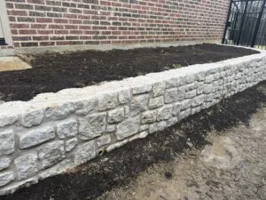 Granbury stone retaining wall along brick home foundation creating level raised bed in Coppell TX backyard