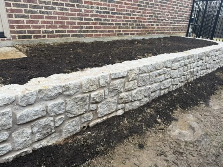 Granbury stone retaining wall along brick home foundation creating level raised bed in Coppell TX backyard