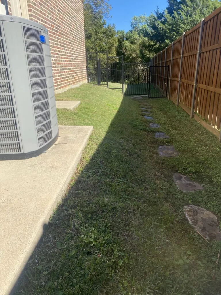 Narrow side yard with stepping stones along wood fence before retaining wall installation to level sloped ground in Coppell TX