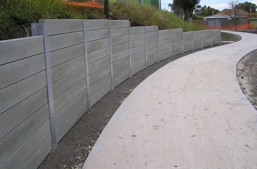 Long curved concrete panel retaining wall holding back sloped hillside beside a winding concrete driveway, Fort Worth TX