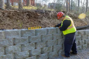 contractor in hard hat and safety vest levels concrete block retaining wall on sloped residential property in DFW