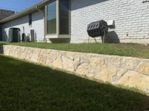 Granbury stone retaining wall along the back of a white brick home, creating a level lawn terrace in Dallas, TX