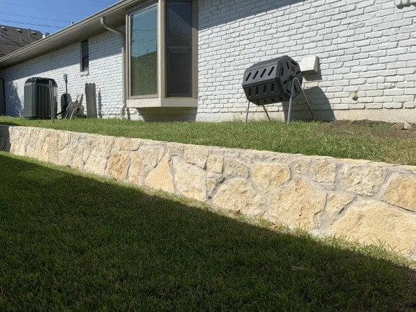 Granbury stone retaining wall along the back of a white brick home, creating a level lawn terrace in Dallas, TX