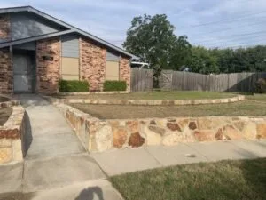 Milsap stone retaining wall lining front yard and walkway of brick home in Grand Prairie, TX, replacing a failing block wall