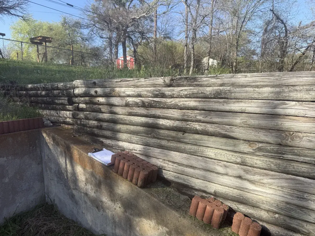 Failing railroad-tie retaining wall in Azle, TX leaning forward with bricks stacked underneath for support before replacement