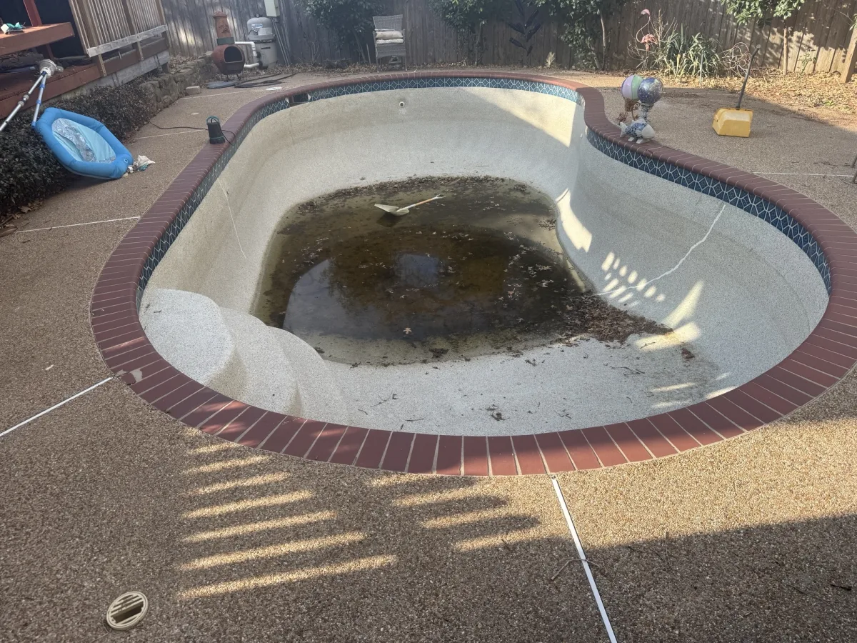 Old kidney-shaped in-ground pool with red brick coping in Bedford, TX before removal by DFW Retaining Walls and Pool Demo