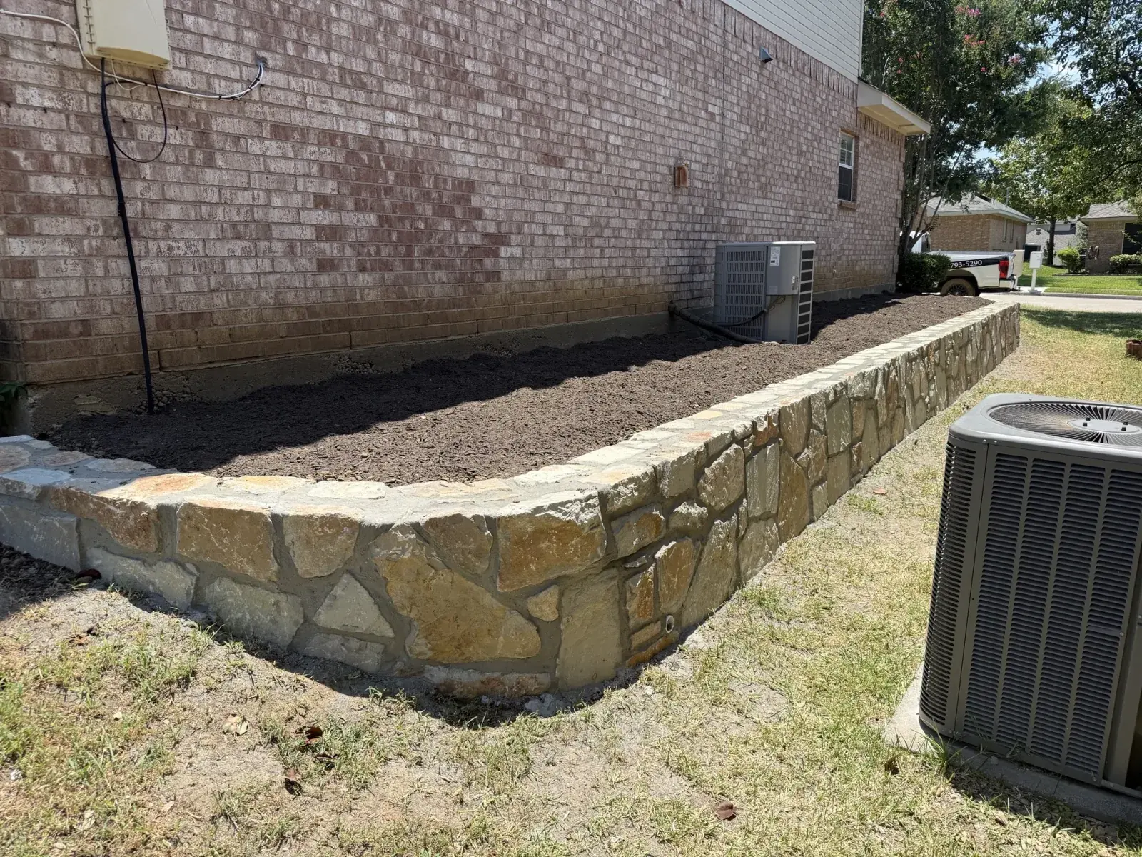 New Millsap stone retaining wall along a Flower Mound, TX home controlling the grade beside the foundation, built by DFW Retaining Walls and Pool Demo