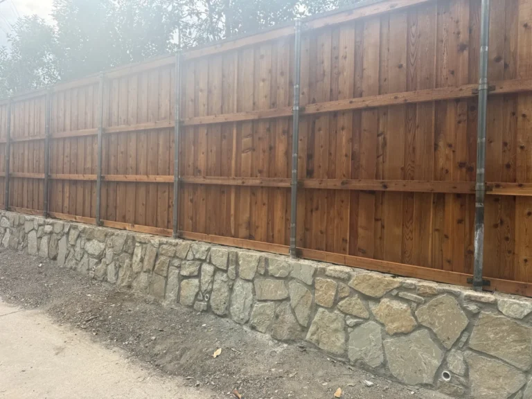 New mortared stone retaining wall with weep holes and an 8-foot cedar fence along an alley in Dallas, TX