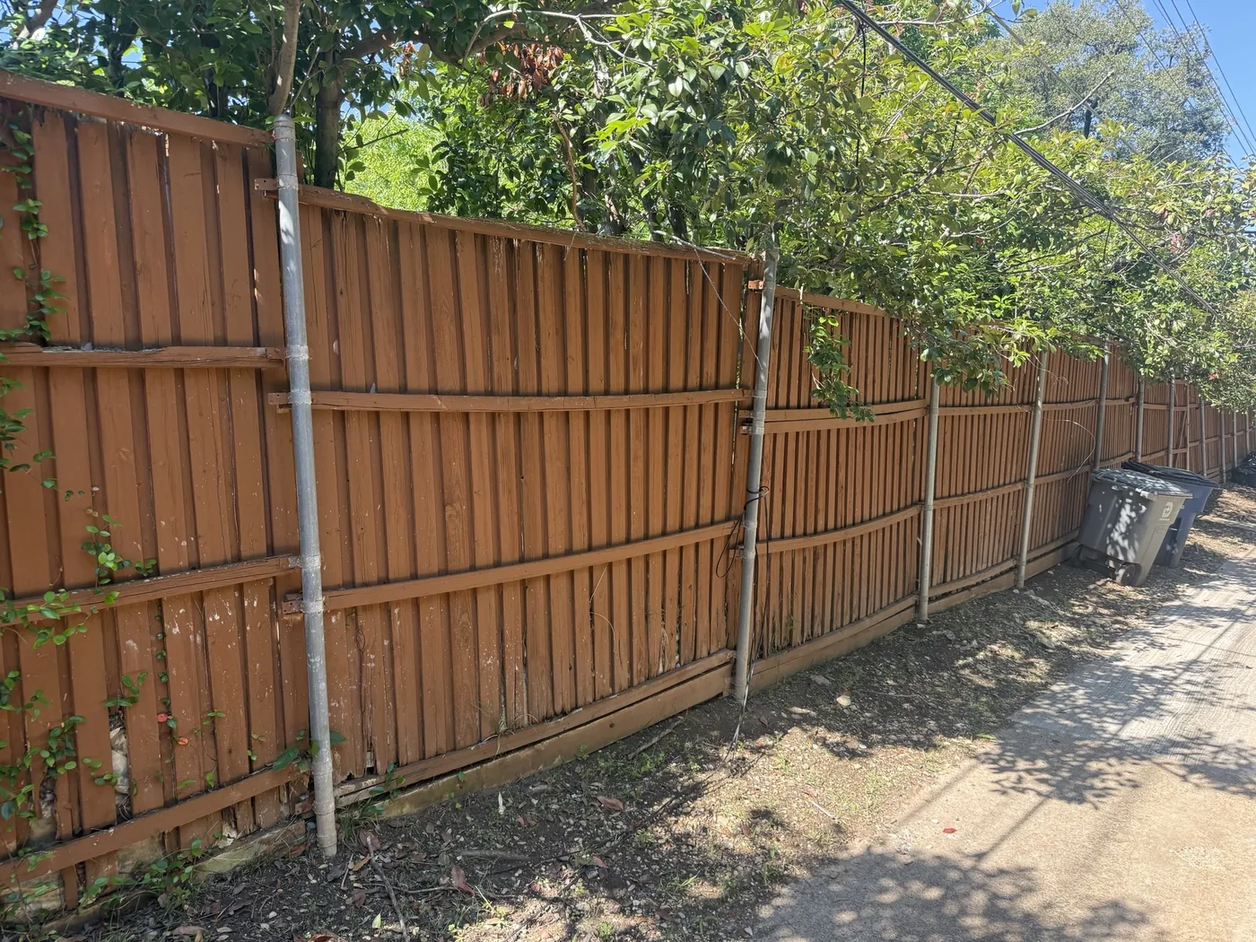 Leaning fence and crosstie wall before replacement — Dallas, TX Weathered, leaning board fence on an old crosstie retaining wall along an alley in Dallas, TX before replacement