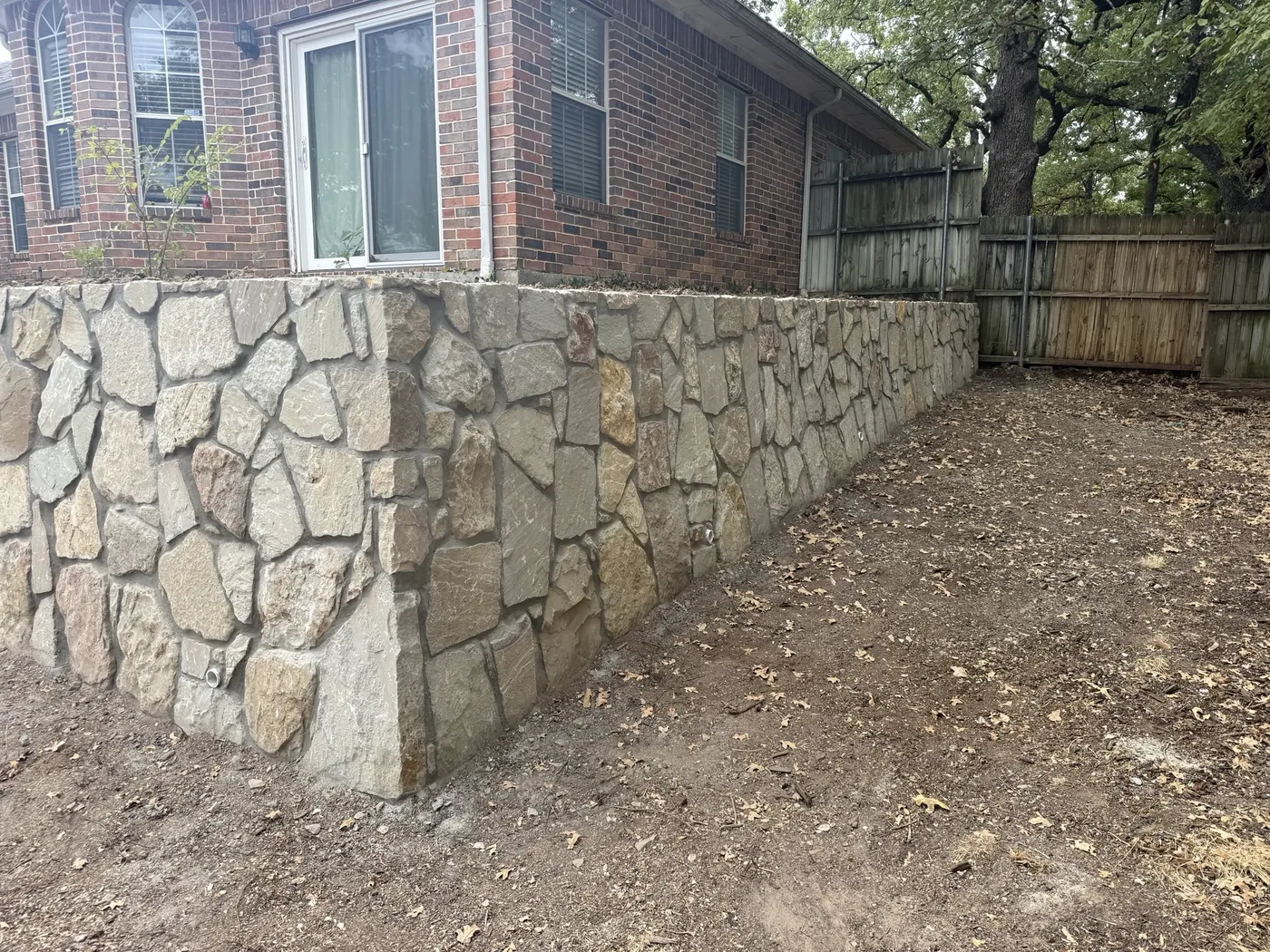 New mortared Milsap stone retaining wall with weep holes along the back of a brick home in Denton, TX