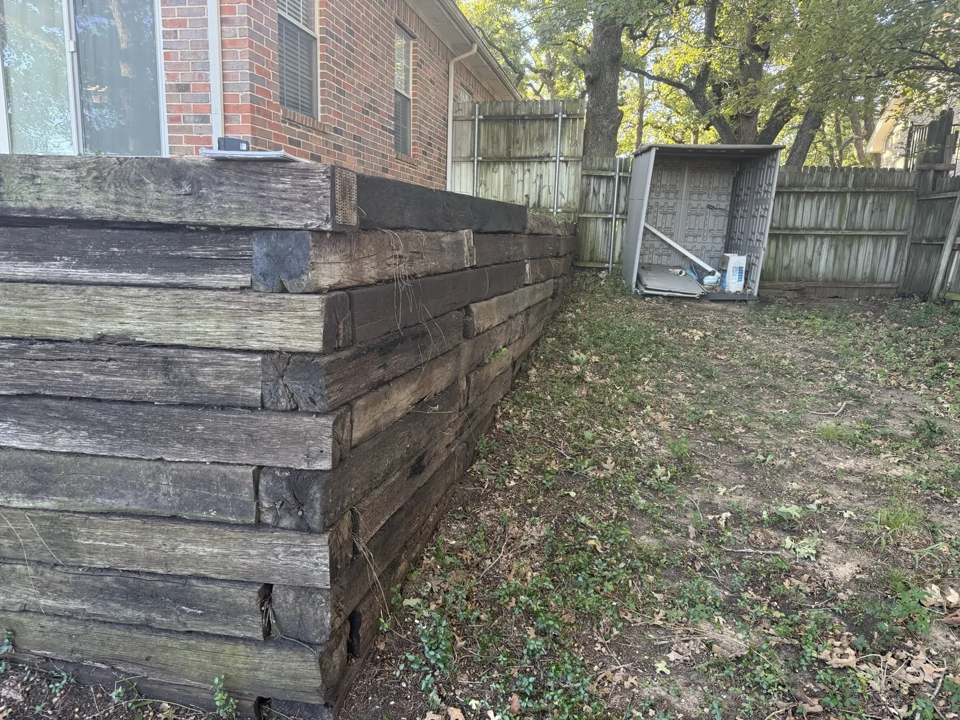 Rotting stacked railroad-tie retaining wall along the back of a brick home in Denton, TX before replacement