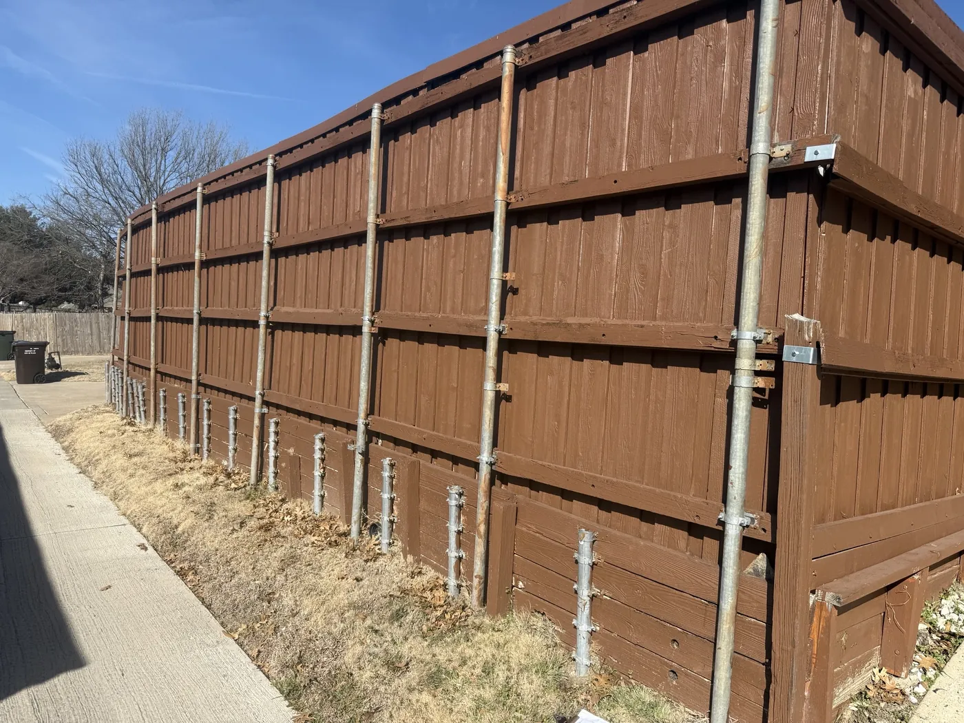 Old 2x4 board retaining wall under a tall wood fence along an alley in Plano, TX before replacement