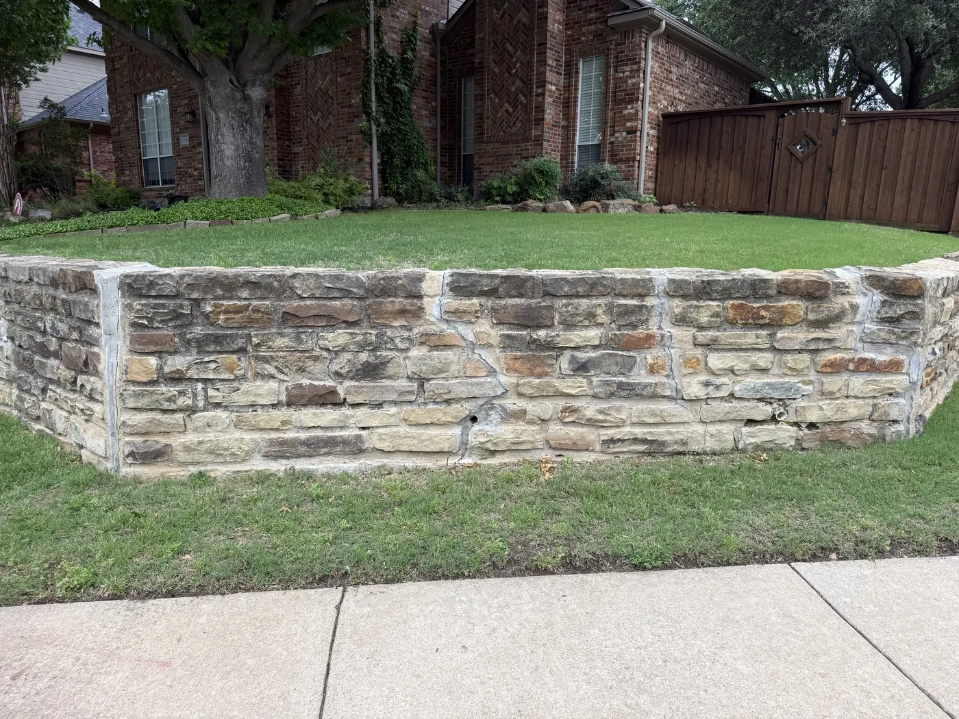 Cracked and bowing chopped-stone retaining wall on a Plano, TX front yard beside the sidewalk before rebuild